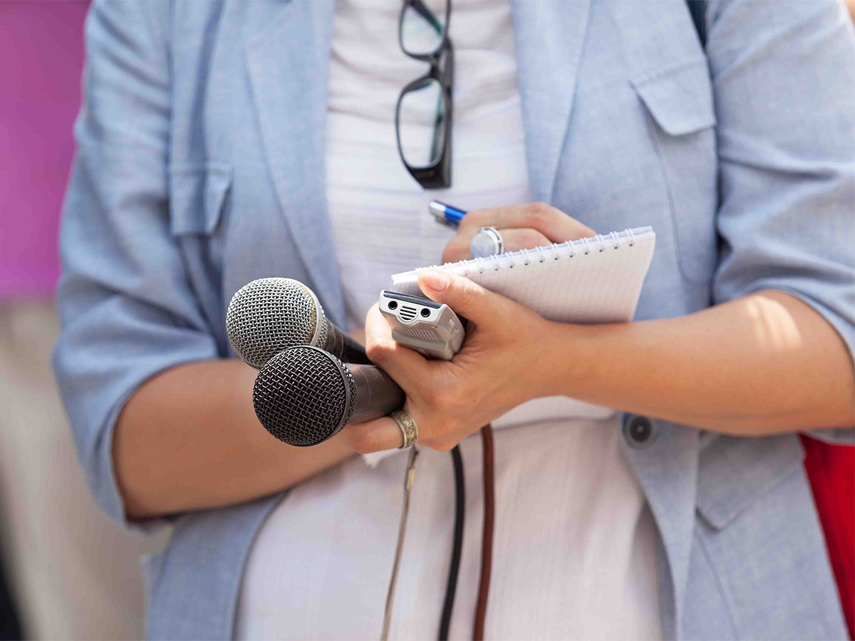 a reporter holding two microphones, a tape recorder and a notepad