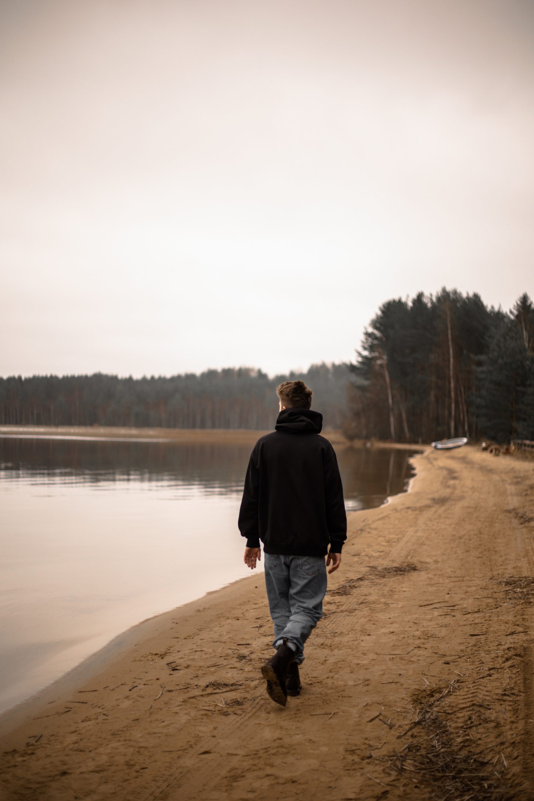 Man in Black Jacket Standing on Brown Sand Near Lake