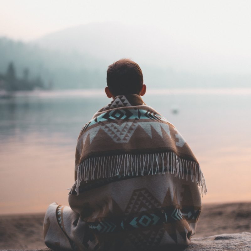 Man Sitting on Sand Facing Body of Water