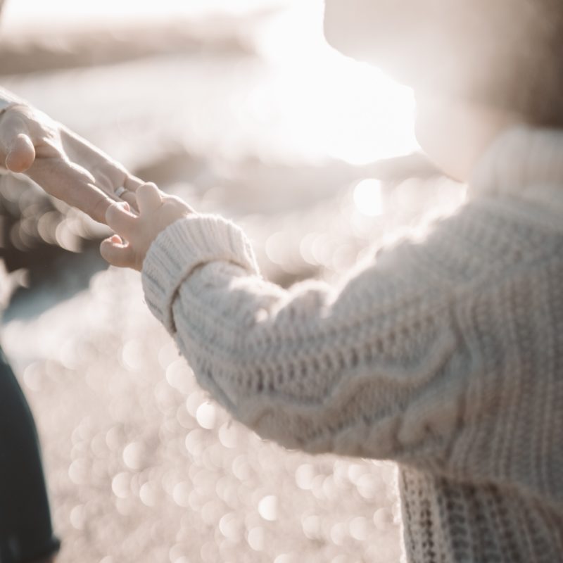 Person in White Knit Sweater Holding Hands With Man in Black Suit Jacket