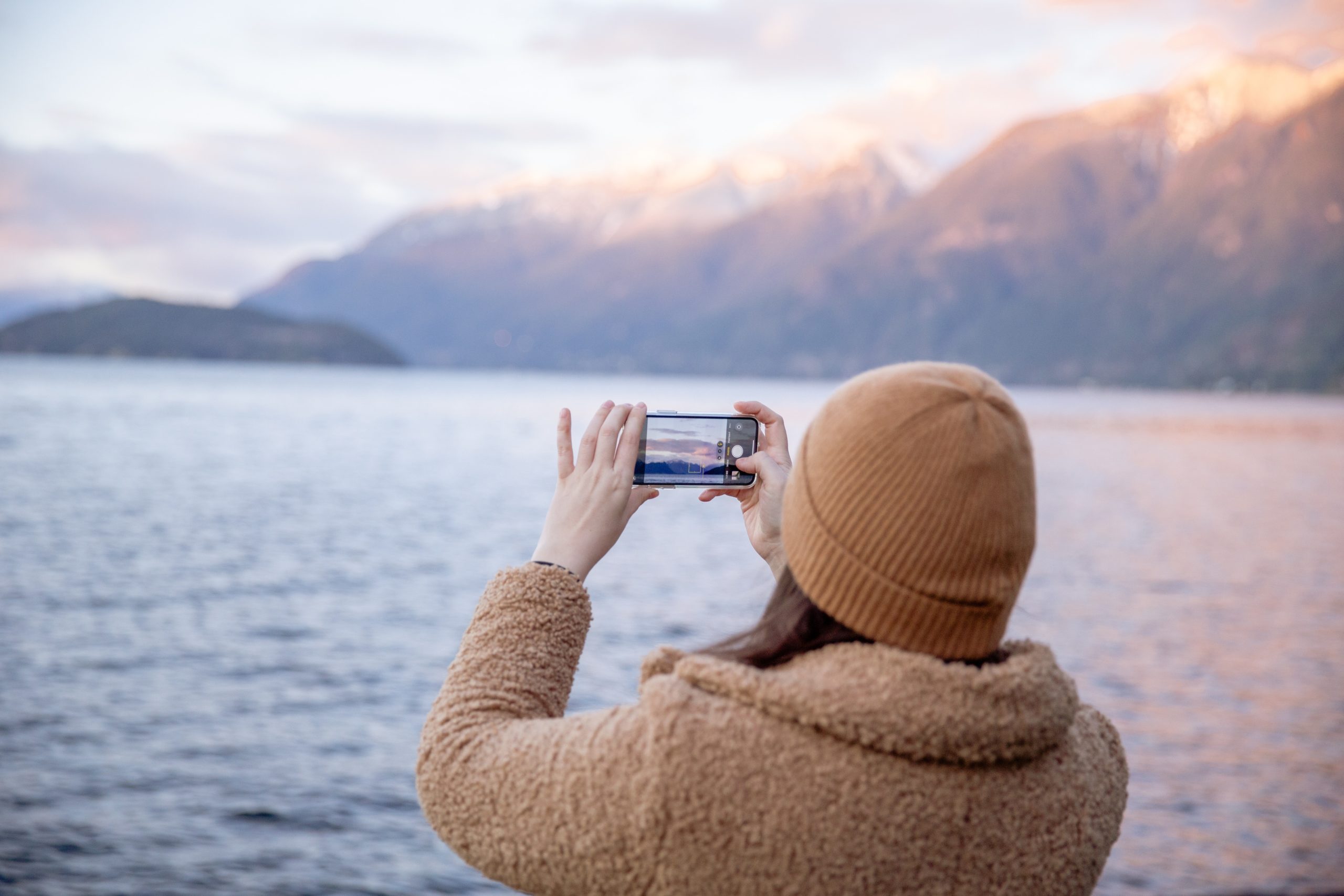 Anonymous female traveler taking photo on smartphone while standing on coast and enjoying seascape